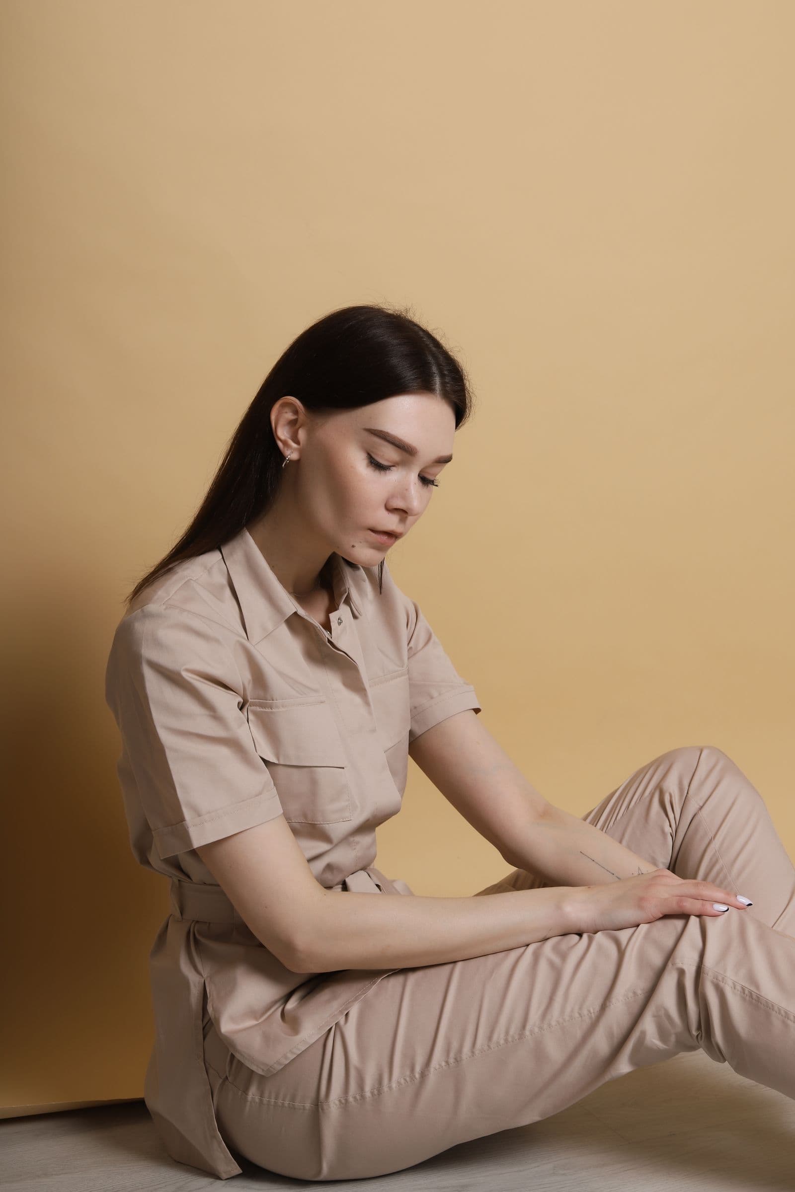 A woman in a beige shirt and trousers against a warm yellow backdrop