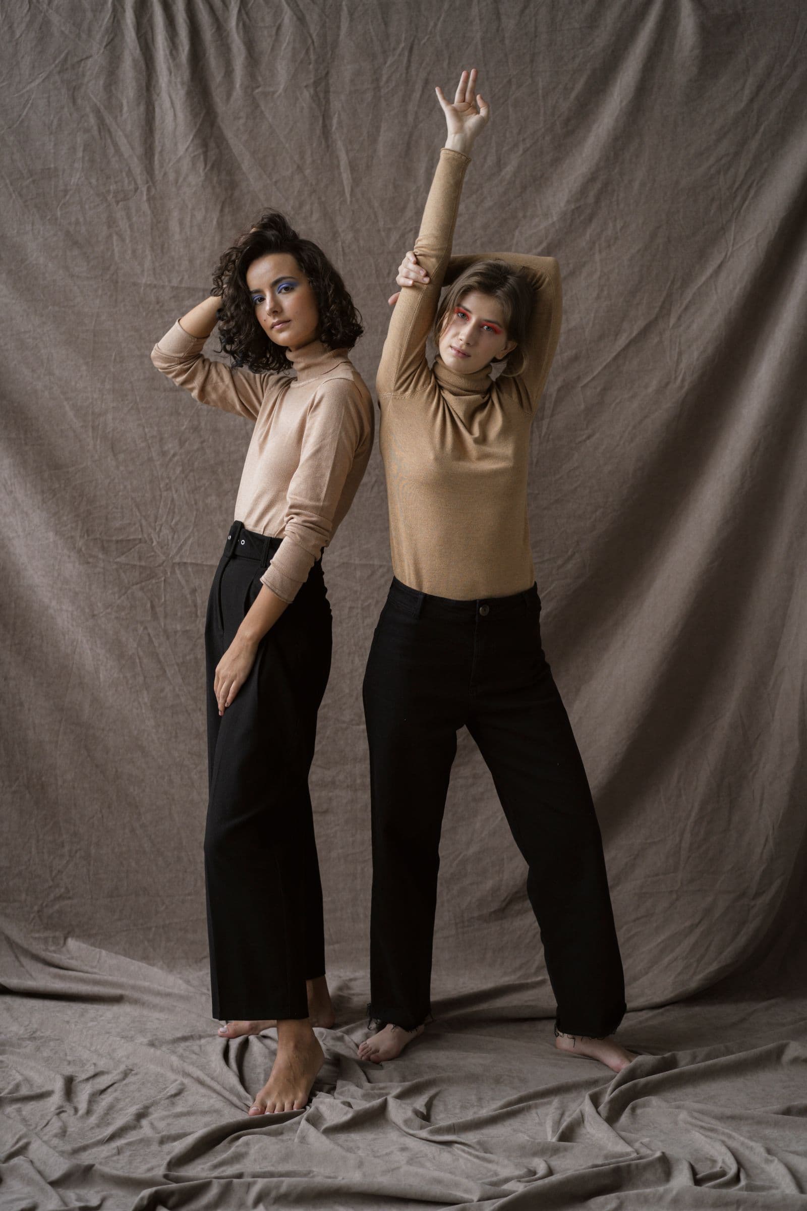 Two models in beige knit tops and black wide trousers
