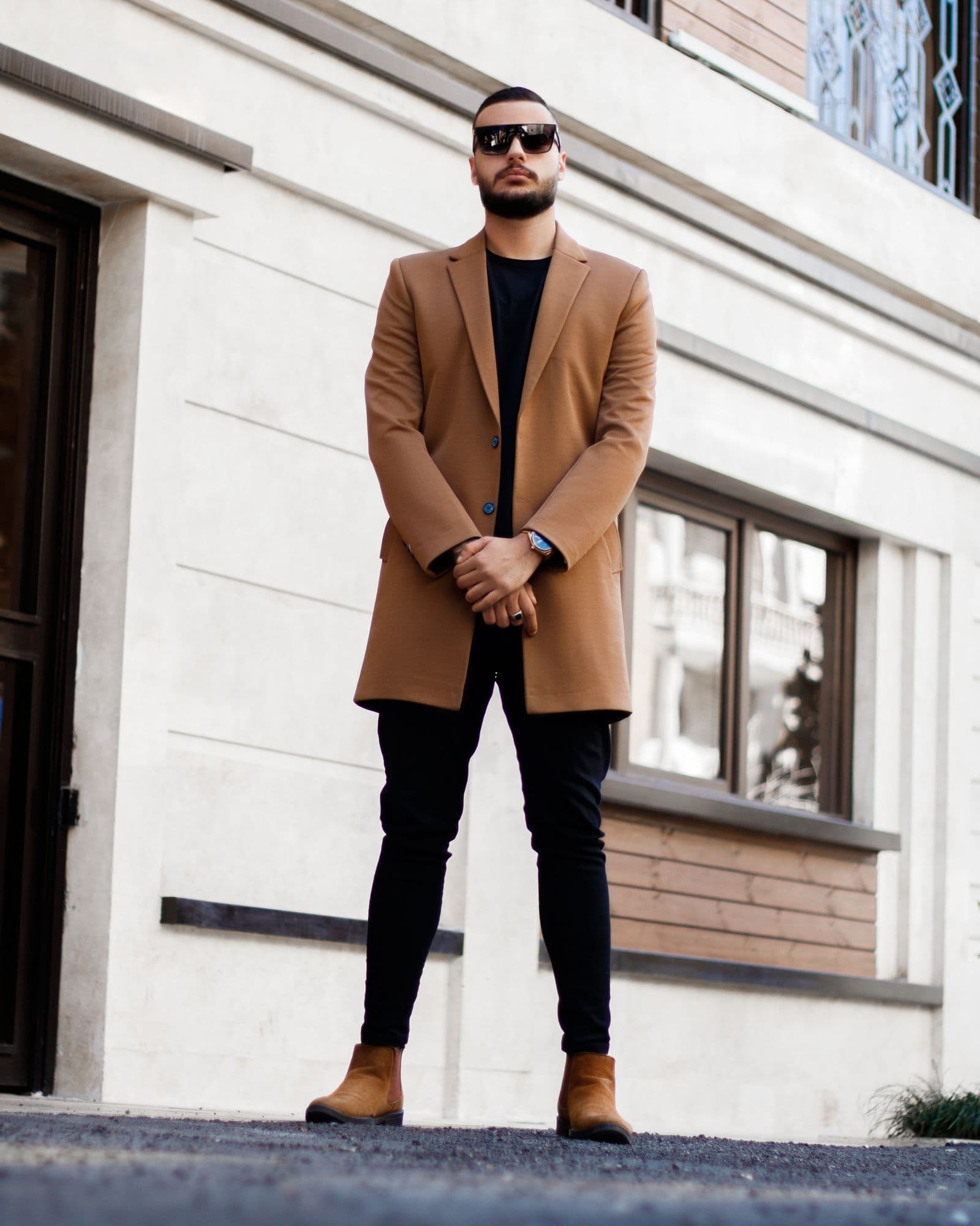 Man in a camel overcoat, black tee and black trousers